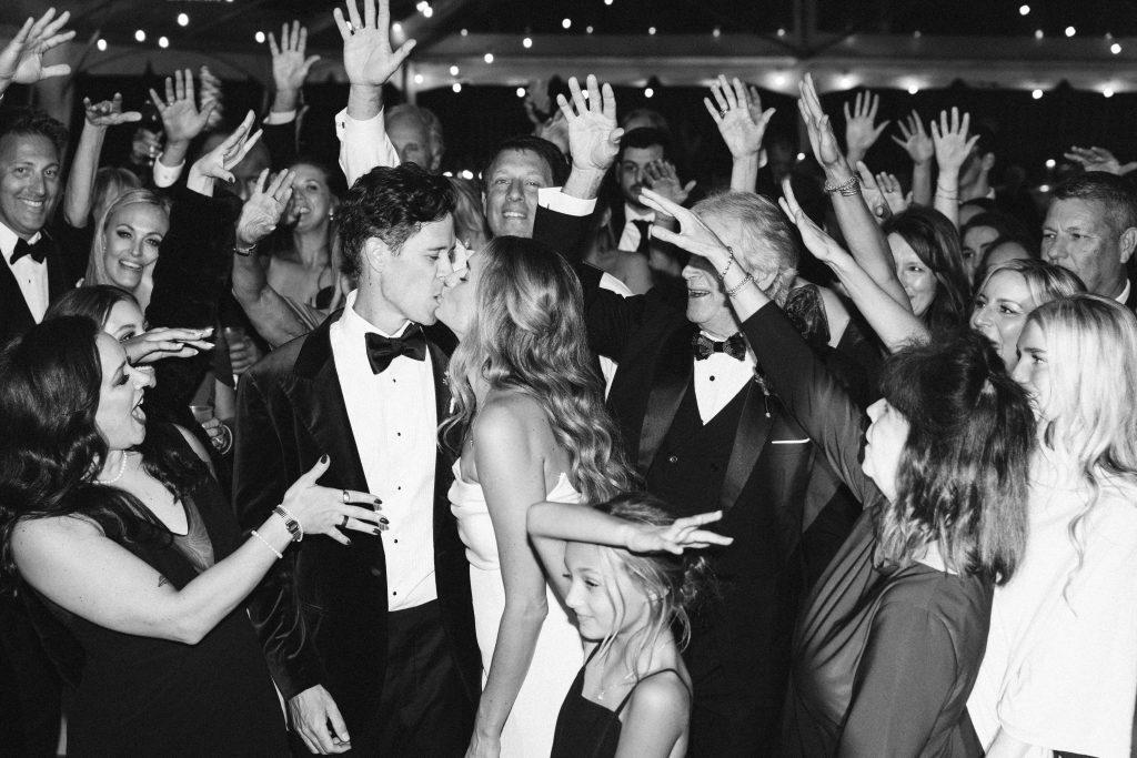 bride and groom kiss as wedding guests celebrate